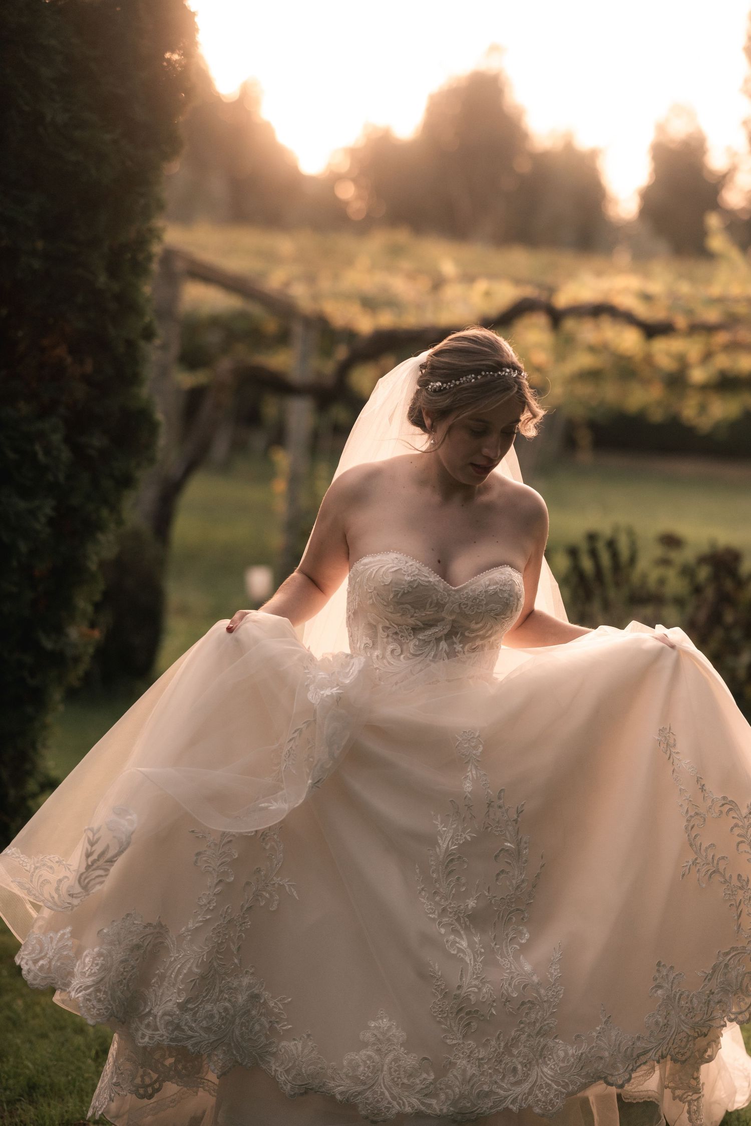 A bride in a strapless lace wedding gown twirls in golden sunset light, making her dress flow elegantly in a garden setting.