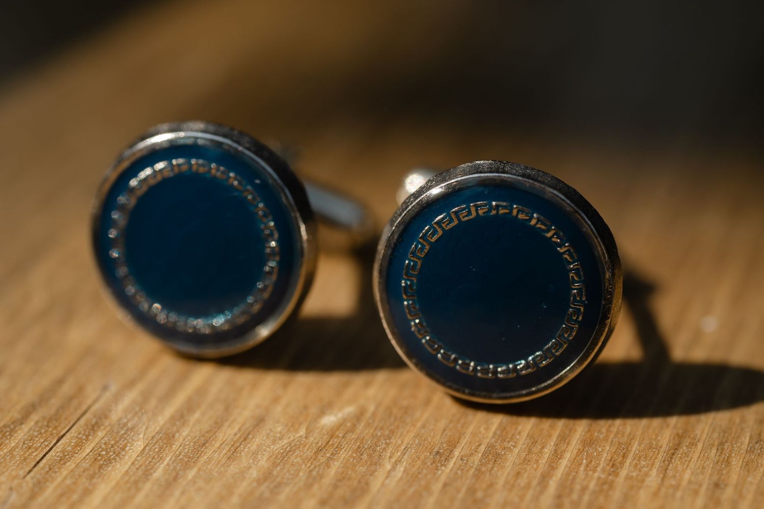 Black cufflinks with intricate detailing shown in a series of close-up macro shots on a wooden surface.