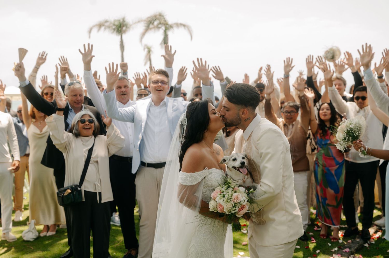 A large group of wedding guests raise their hands in celebration during an outdoor reception.
