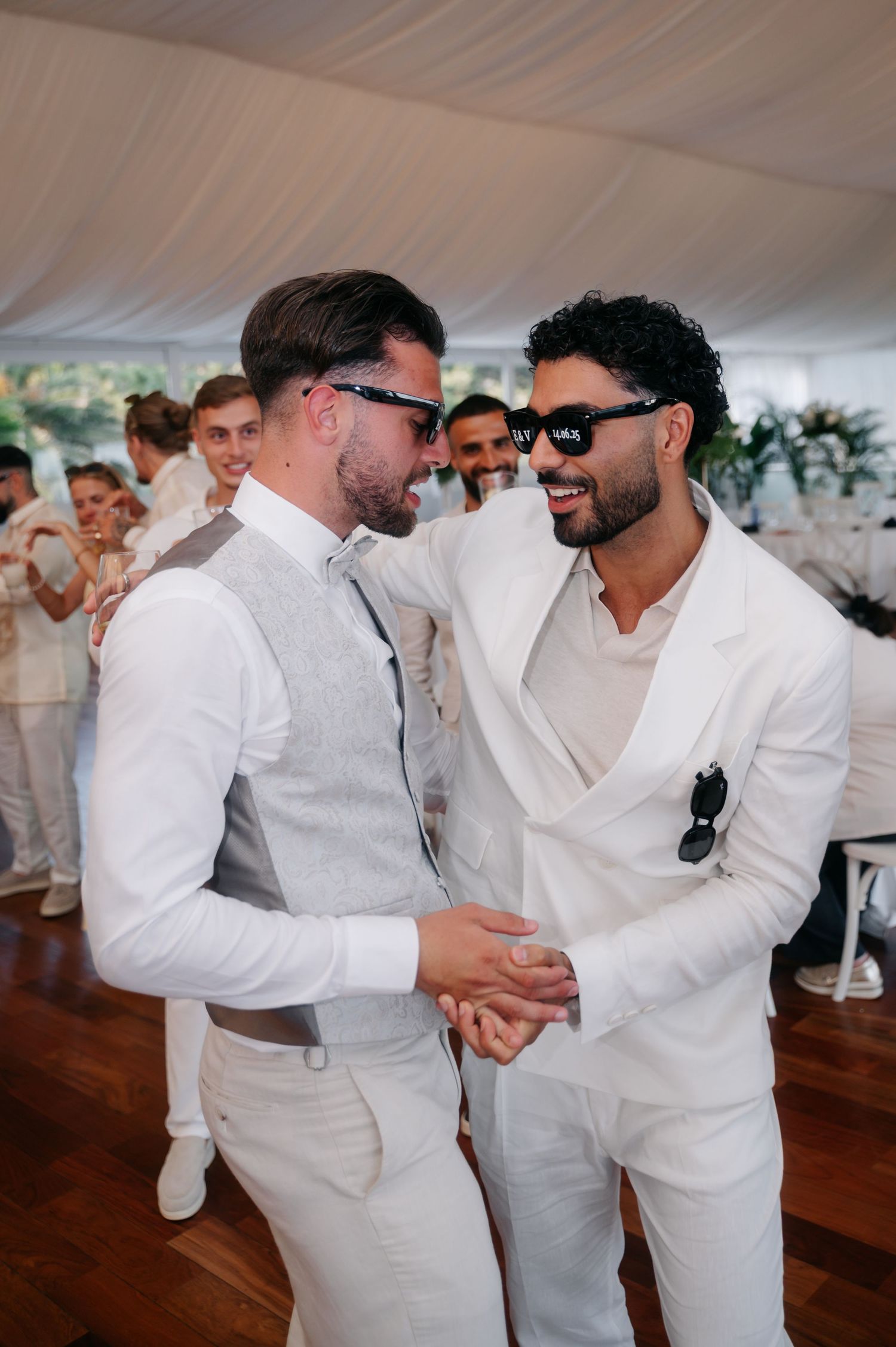 Wedding guests in all-white attire greet and embrace each other during a celebration.