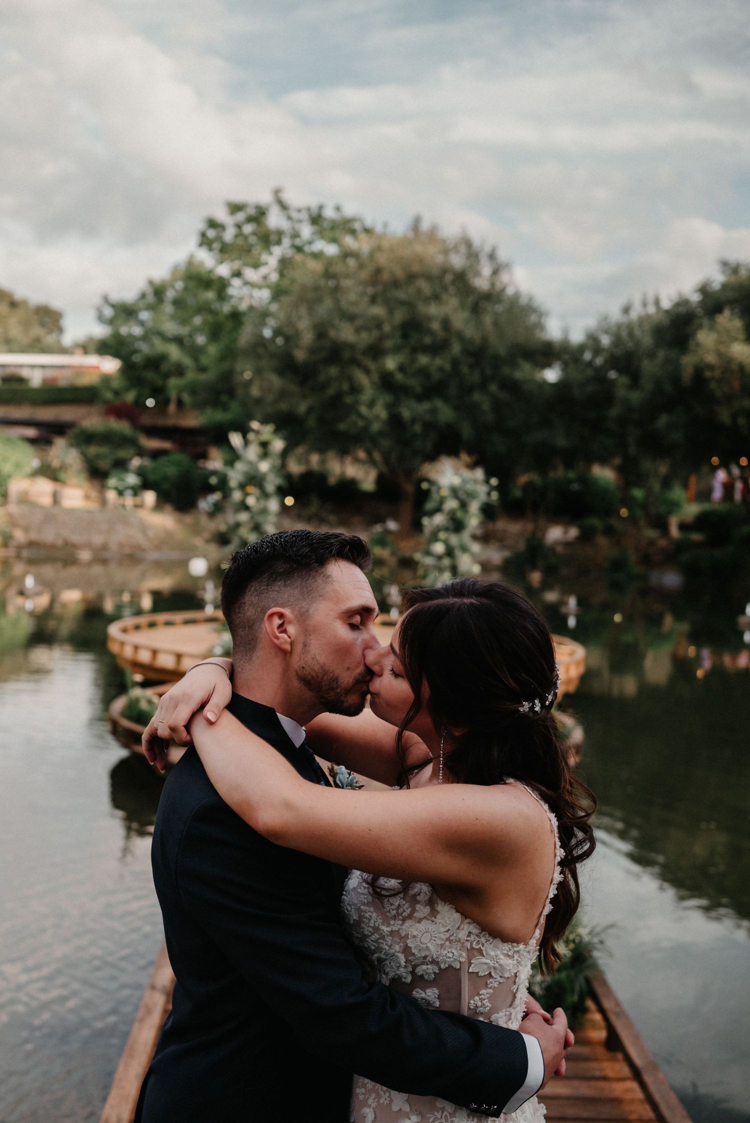 A couple shares passionate kisses by a tranquil lake during their wedding photoshoot.