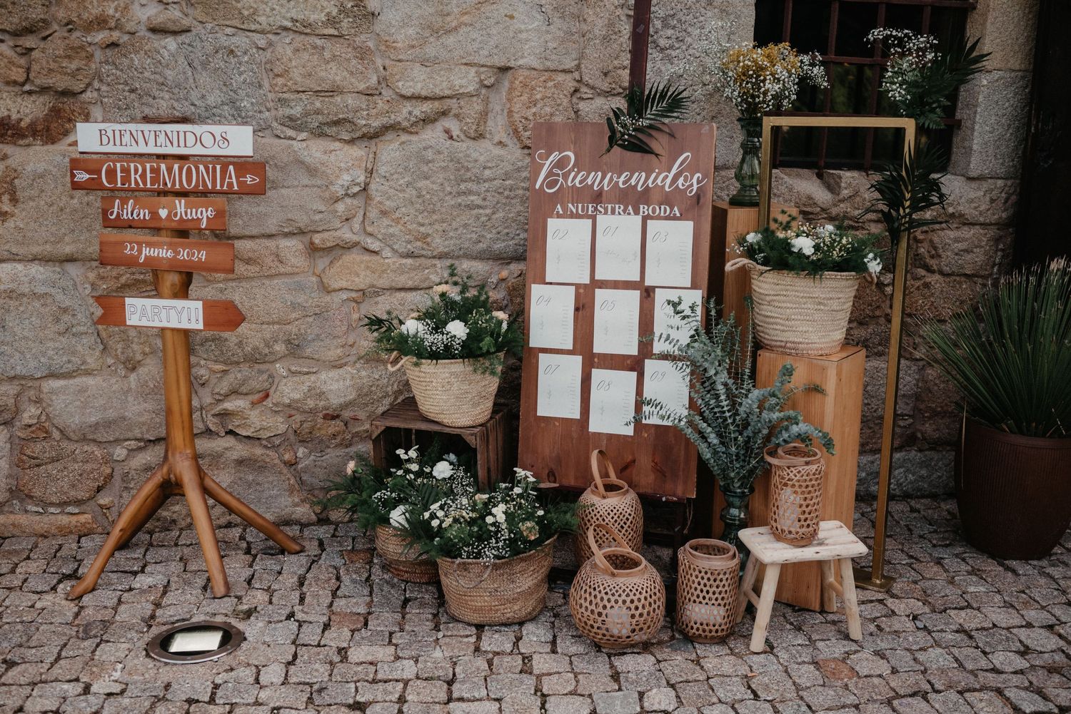 Rustic wedding decor elements including wooden signs, seating charts, and floral arrangements against a stone wall.