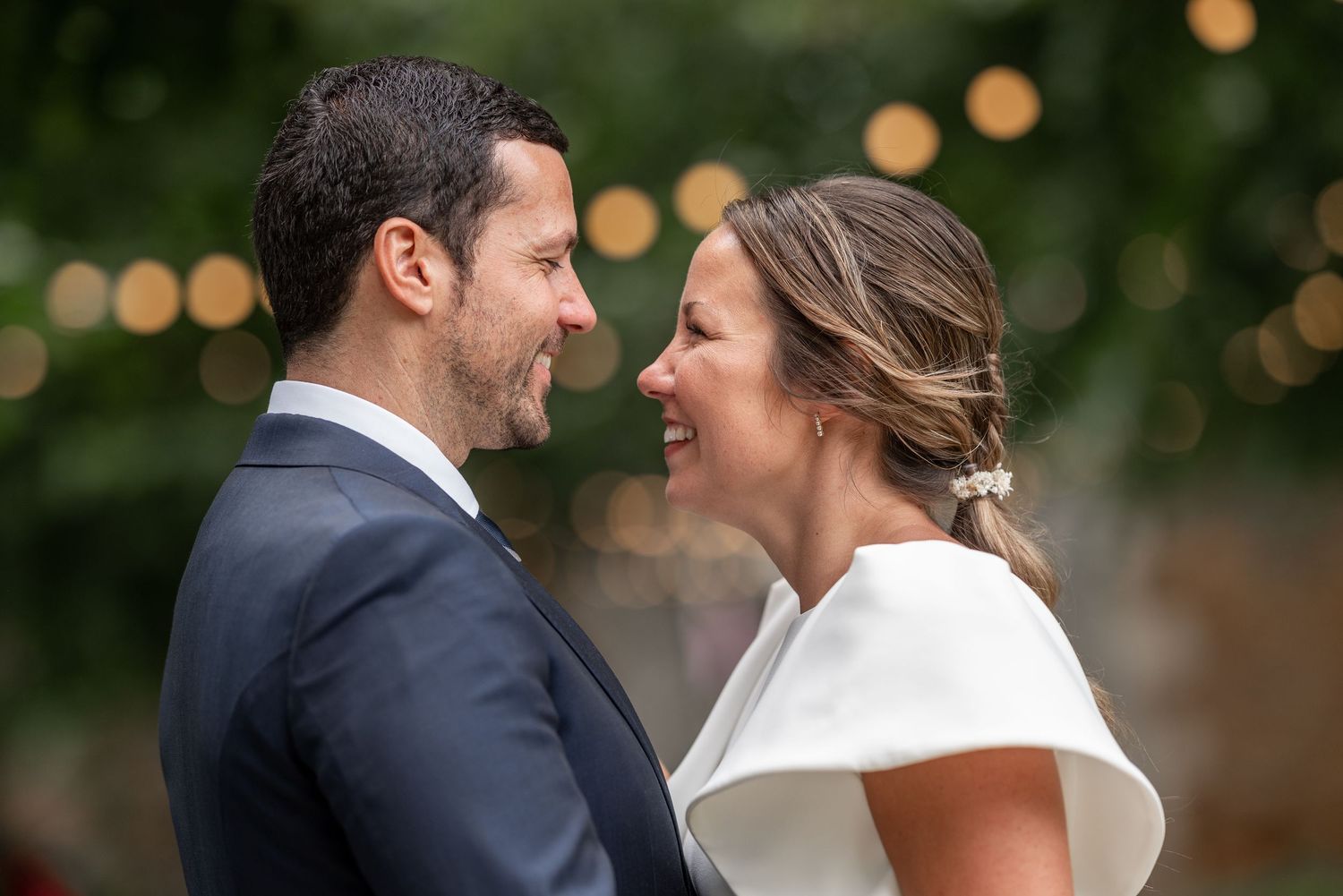 A couple shares a romantic moment during their wedding day with soft bokeh lights in the background.