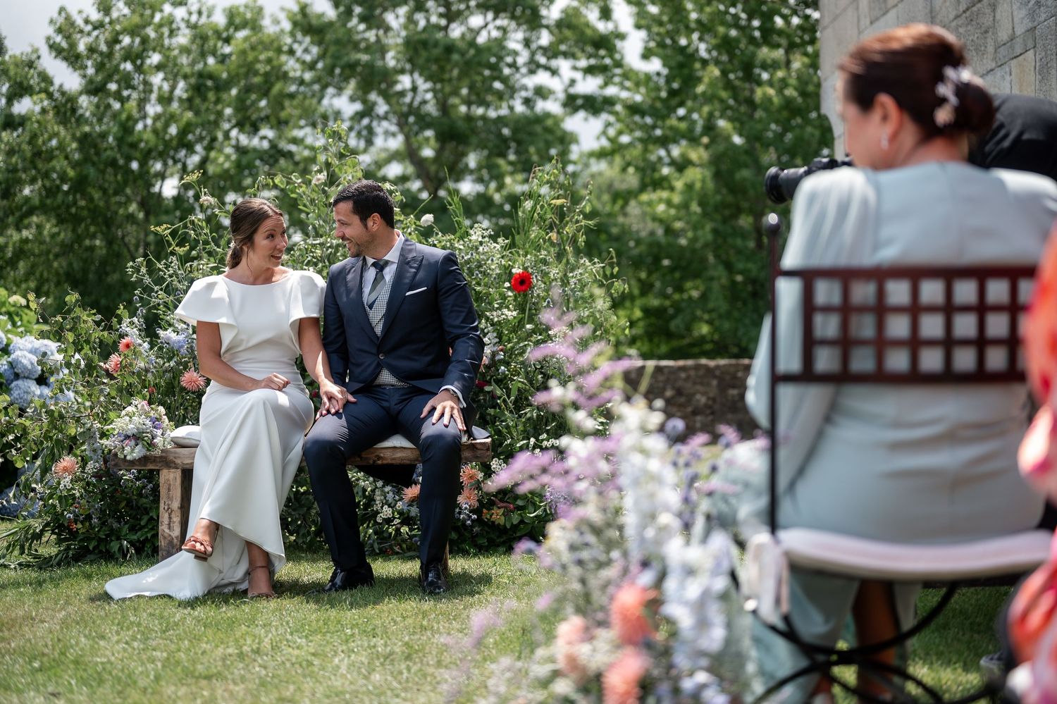 Wedding couple enjoying a relaxed moment in a garden with blooming flowers and natural scenery.