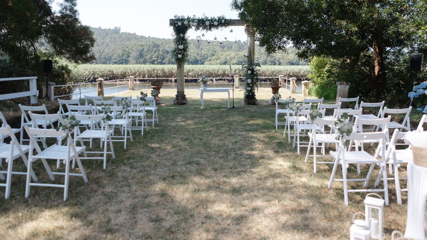 Outdoor wedding ceremony setup with white folding chairs and a floral arch overlooking a scenic countryside view.
