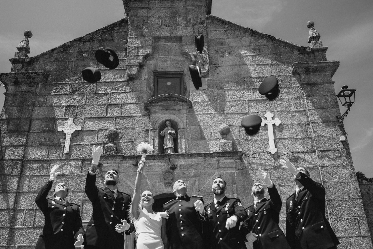 Black and white photo captures military wedding celebration in front of historic stone fortress wall.