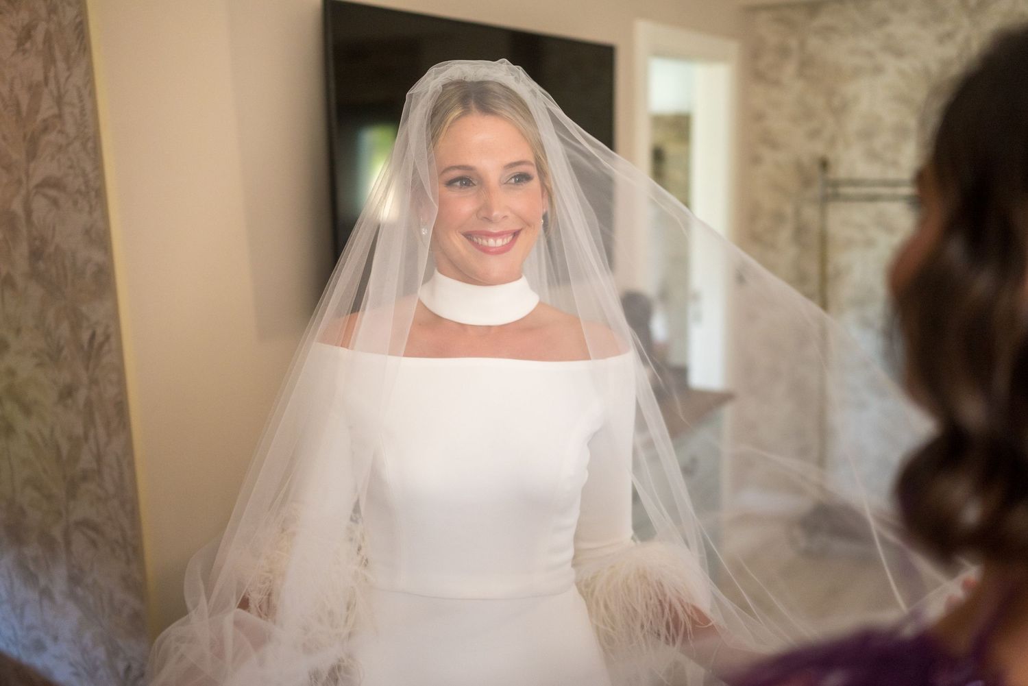 Close up view of bride wearing classic white dress with long flowing veil against neutral background.