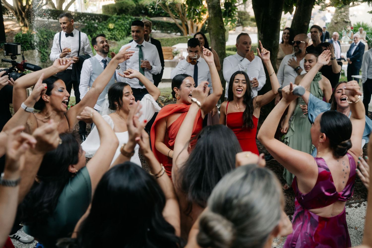 A lively group of wedding guests dancing and celebrating together at an outdoor reception venue.