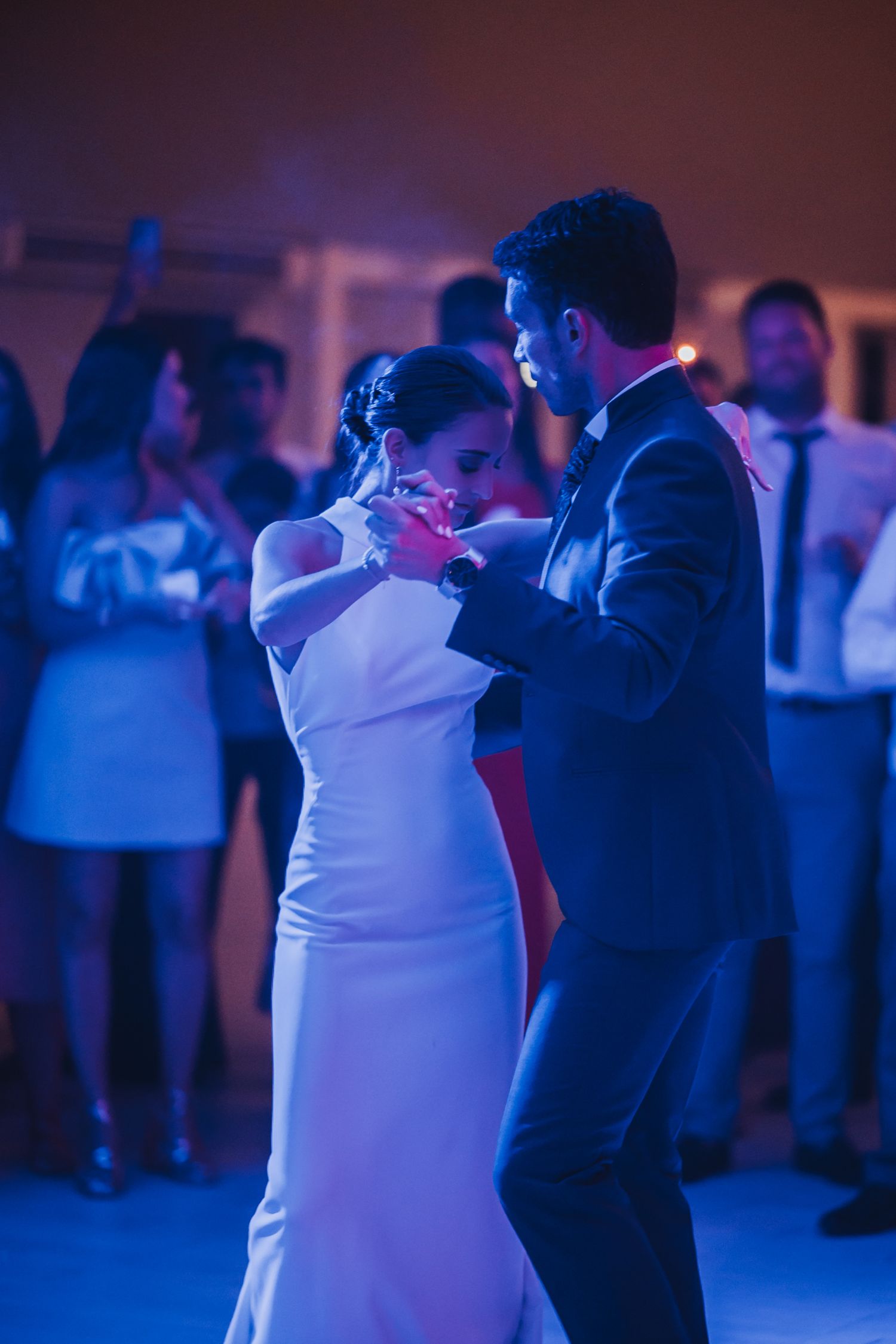 Couples slow dancing together at a wedding reception with blue mood lighting creating a romantic atmosphere.