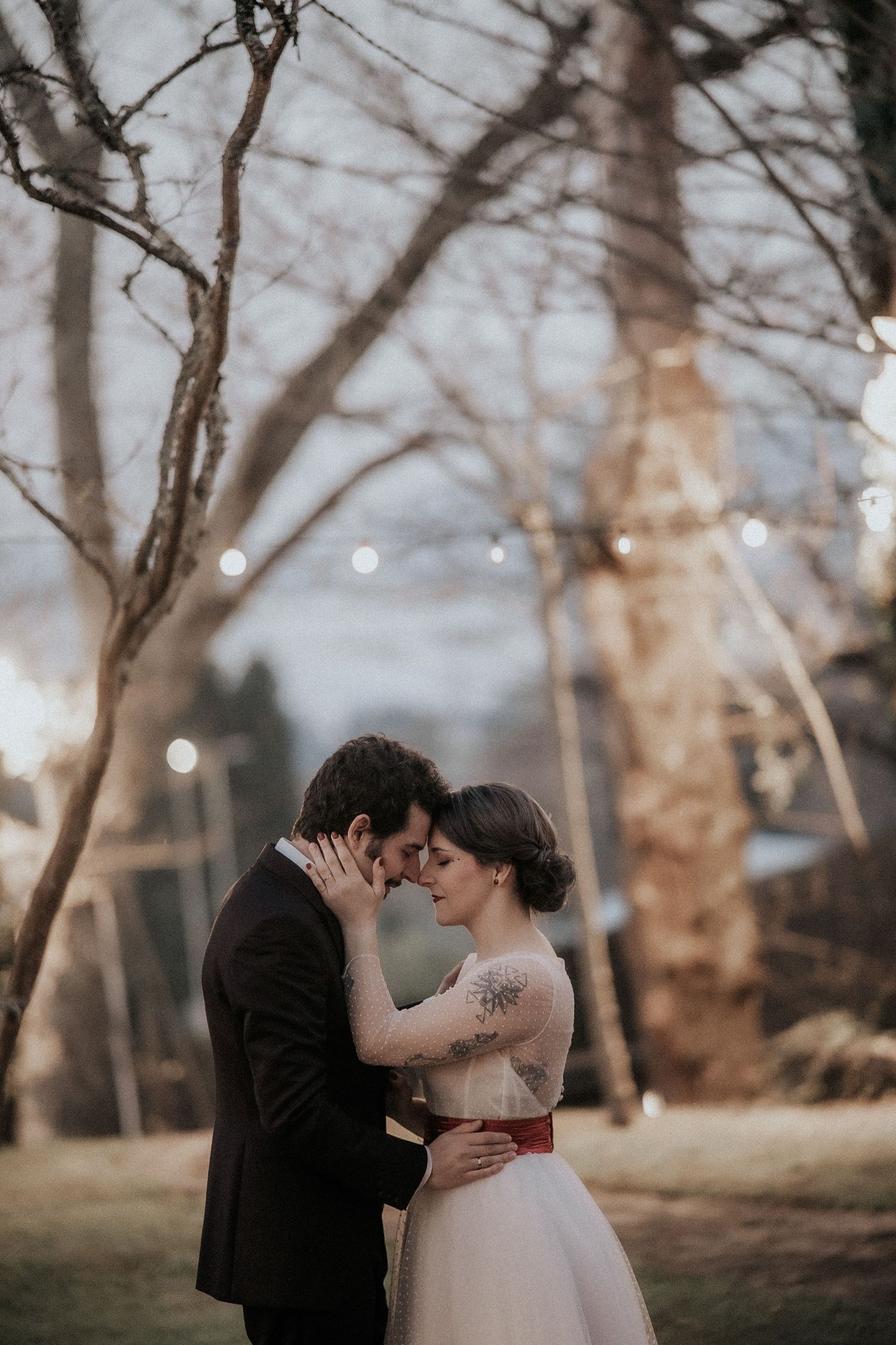 A romantic couple shares intimate moments in a dreamy outdoor setting with trees and soft lighting in the background.