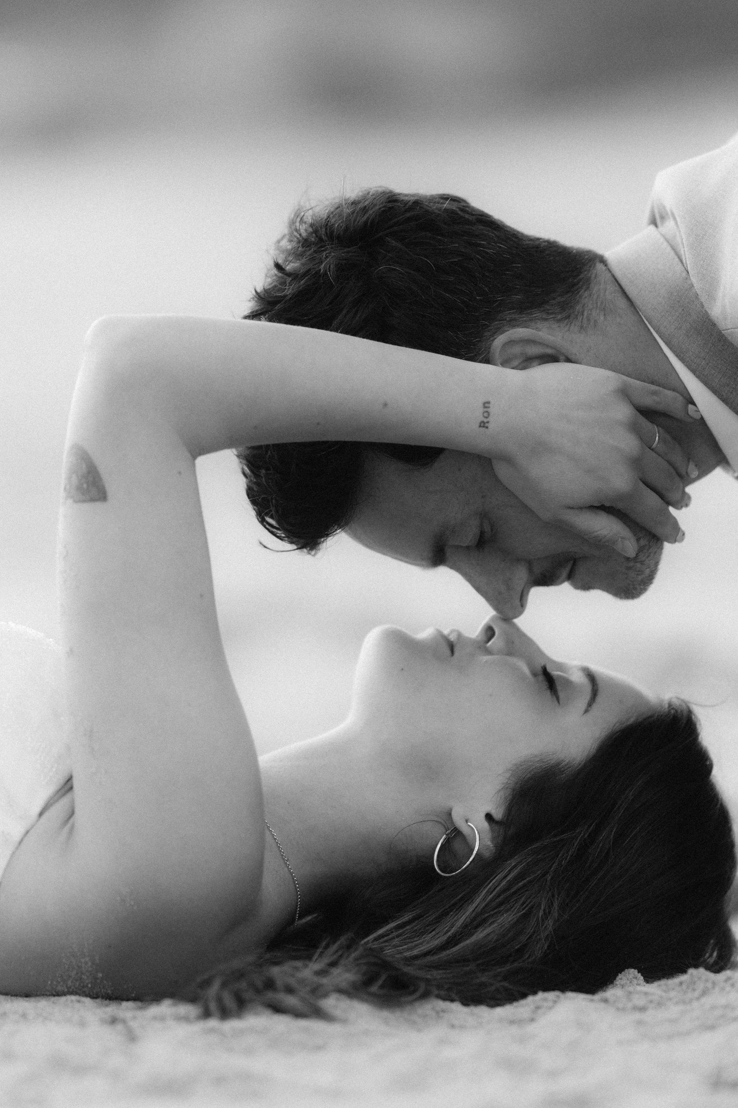 Black and white photo of a romantic couple sharing a tender kiss on a sandy beach.