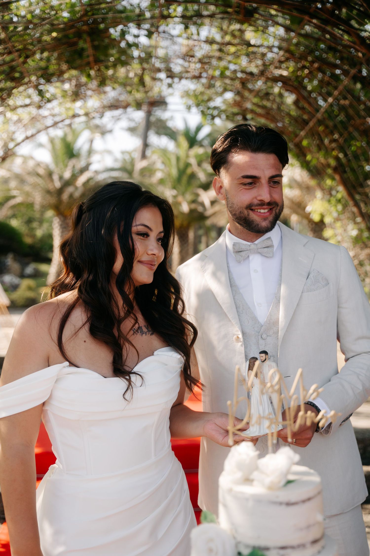 A romantic wedding couple shares intimate moments while cutting their cake in an outdoor garden setting.