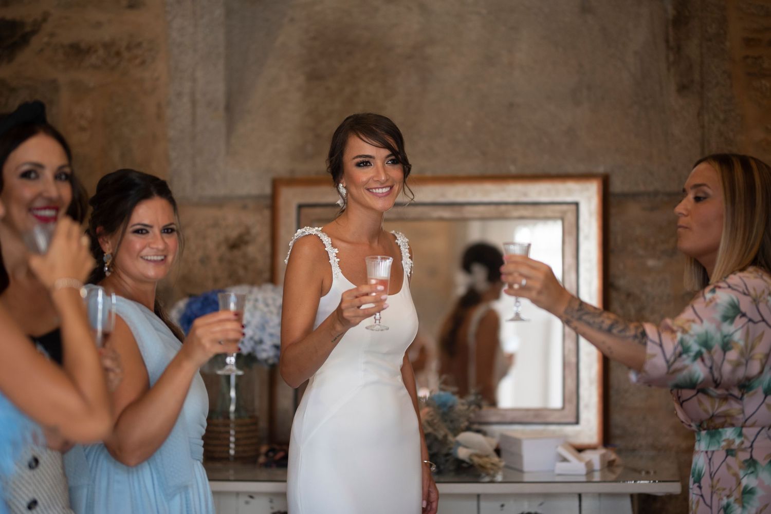 Wedding party getting ready in rustic stone room with natural light streaming through windows.