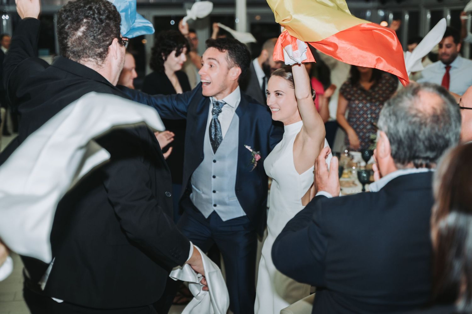 Wedding guests celebrate and wave handkerchiefs during a lively reception party.