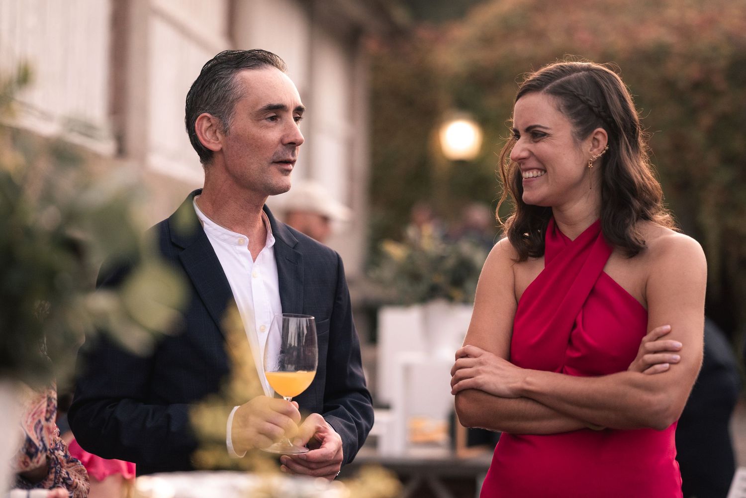 A couple engaged in conversation at an elegant outdoor evening event with wine glasses.