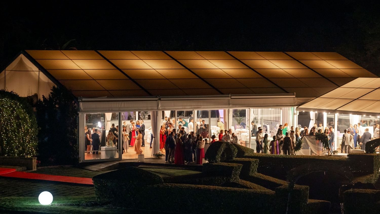 An illuminated wedding reception tent glows warmly against the night sky as guests celebrate inside.