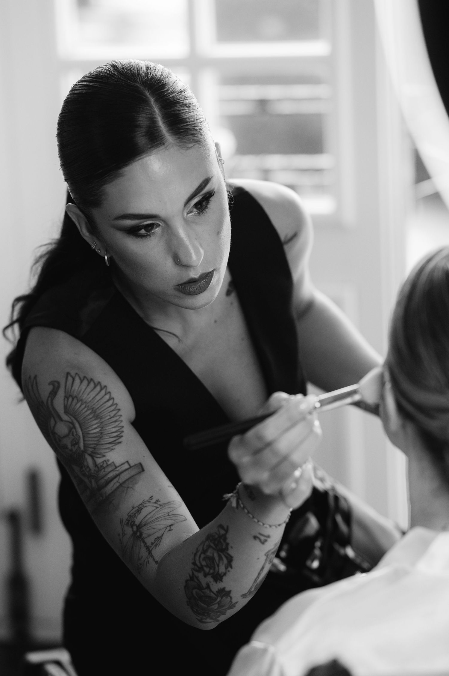 Professional makeup artist with tattoos working intently in black and white portrait.