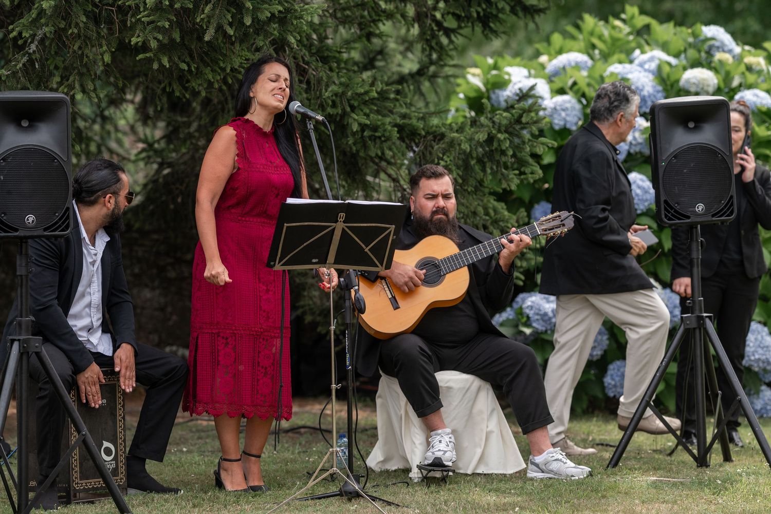 Musicians perform outdoors at a garden event with acoustic guitars and instruments.