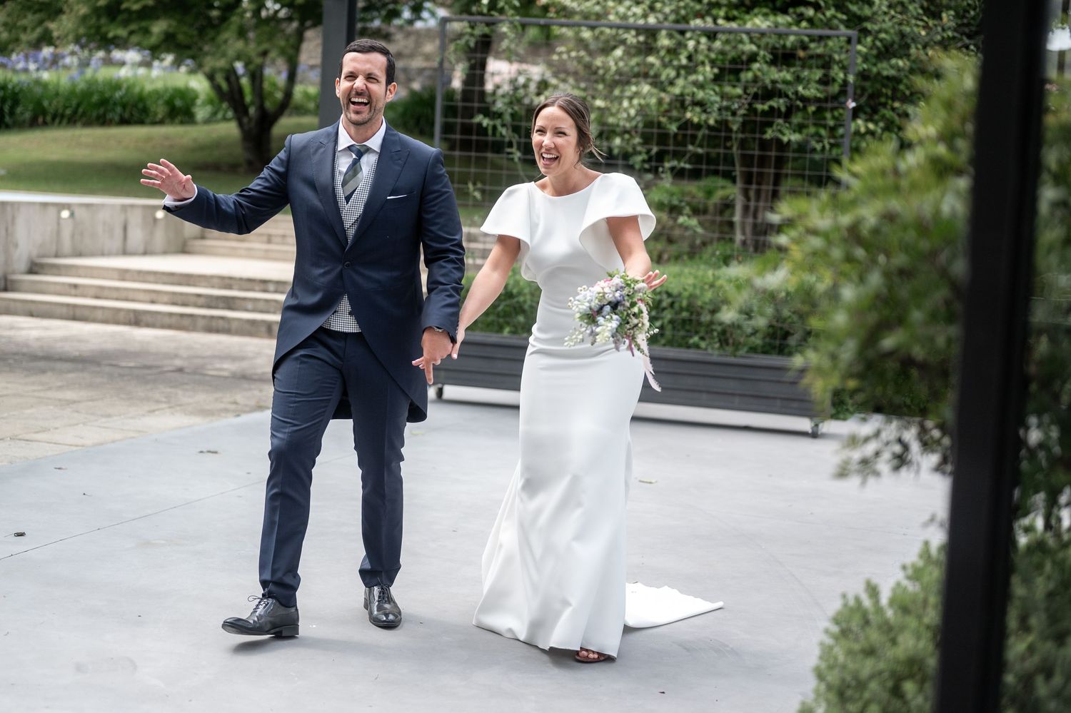 A couple in wedding attire walks together on a path during an outdoor celebration.