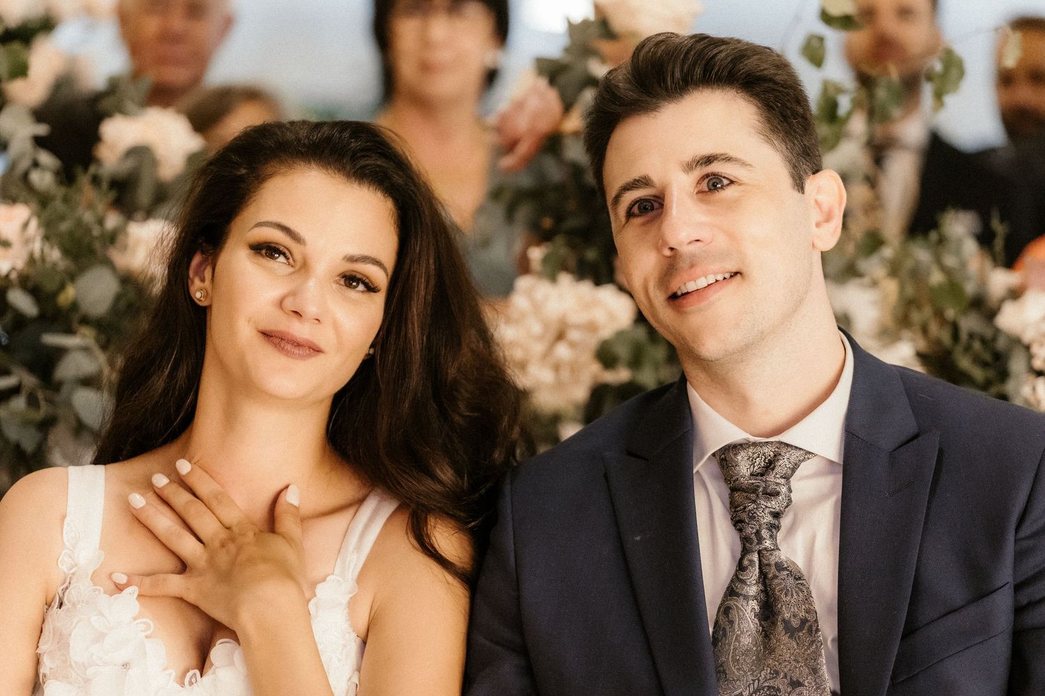 A tender wedding ceremony moment with floral decorations in the background.