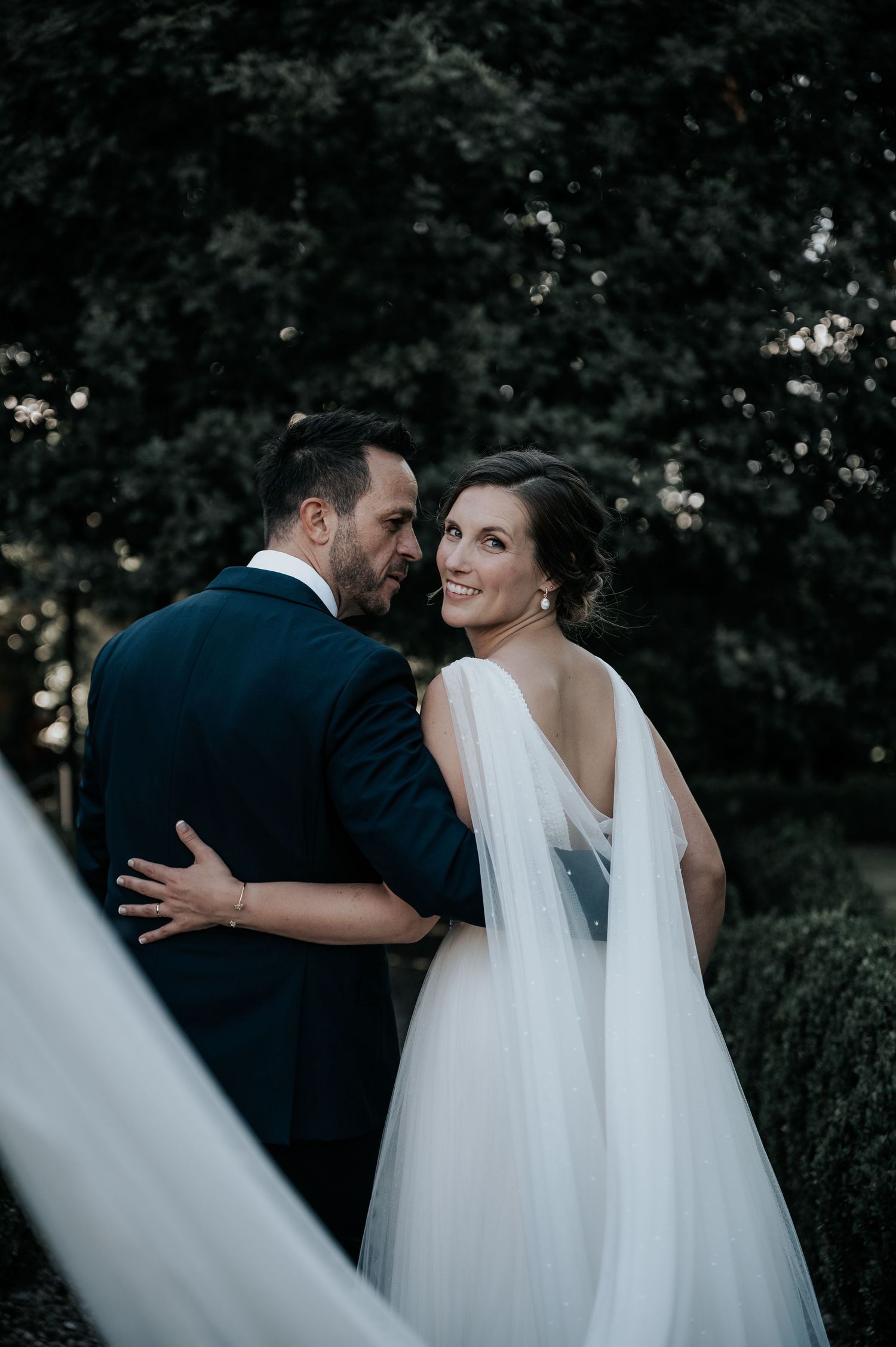 A romantic moment between newlyweds as they embrace outdoors in formal wedding attire during golden hour.