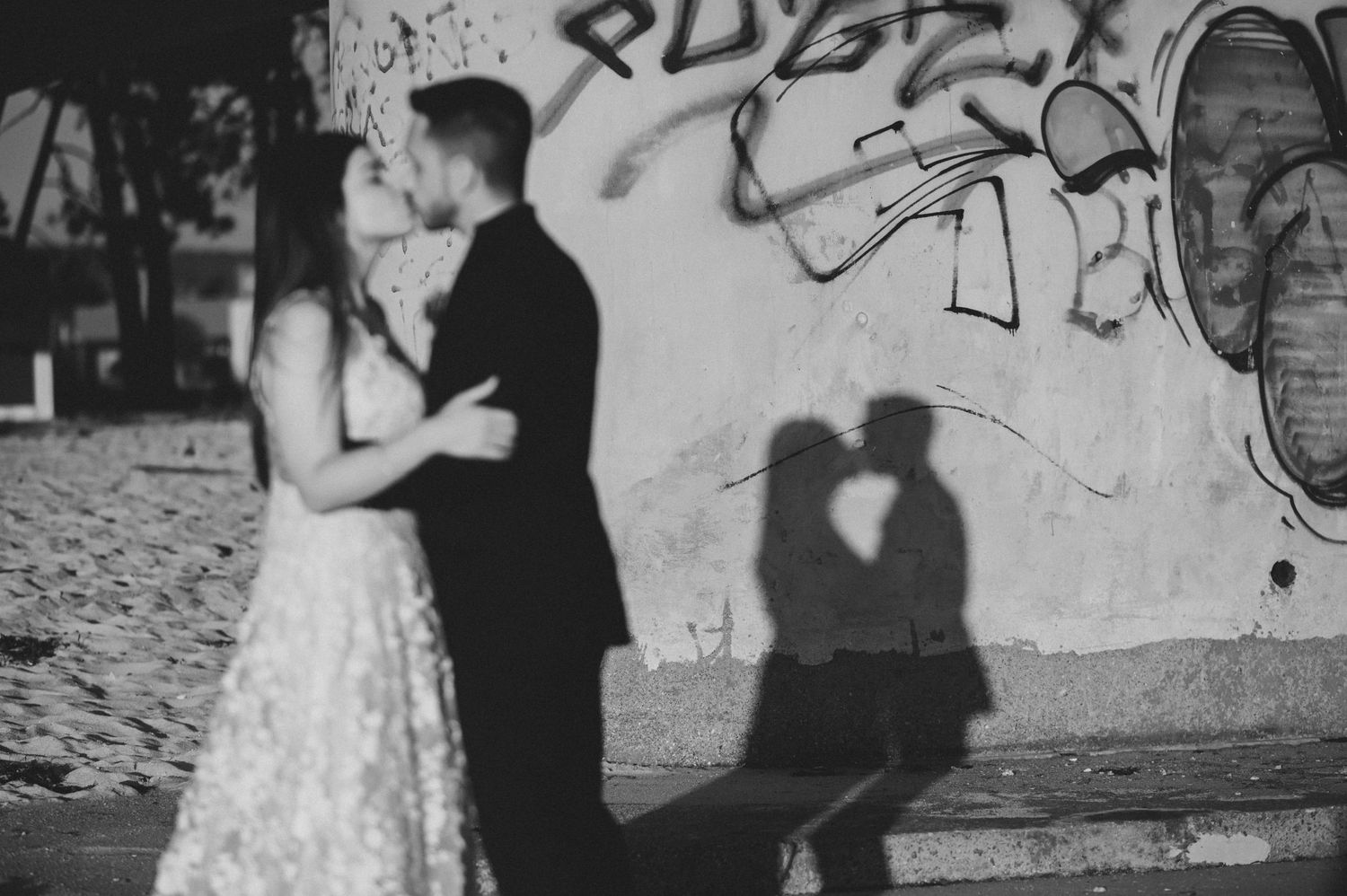 Black and white photos of a couple posing against a graffiti wall in an urban setting.