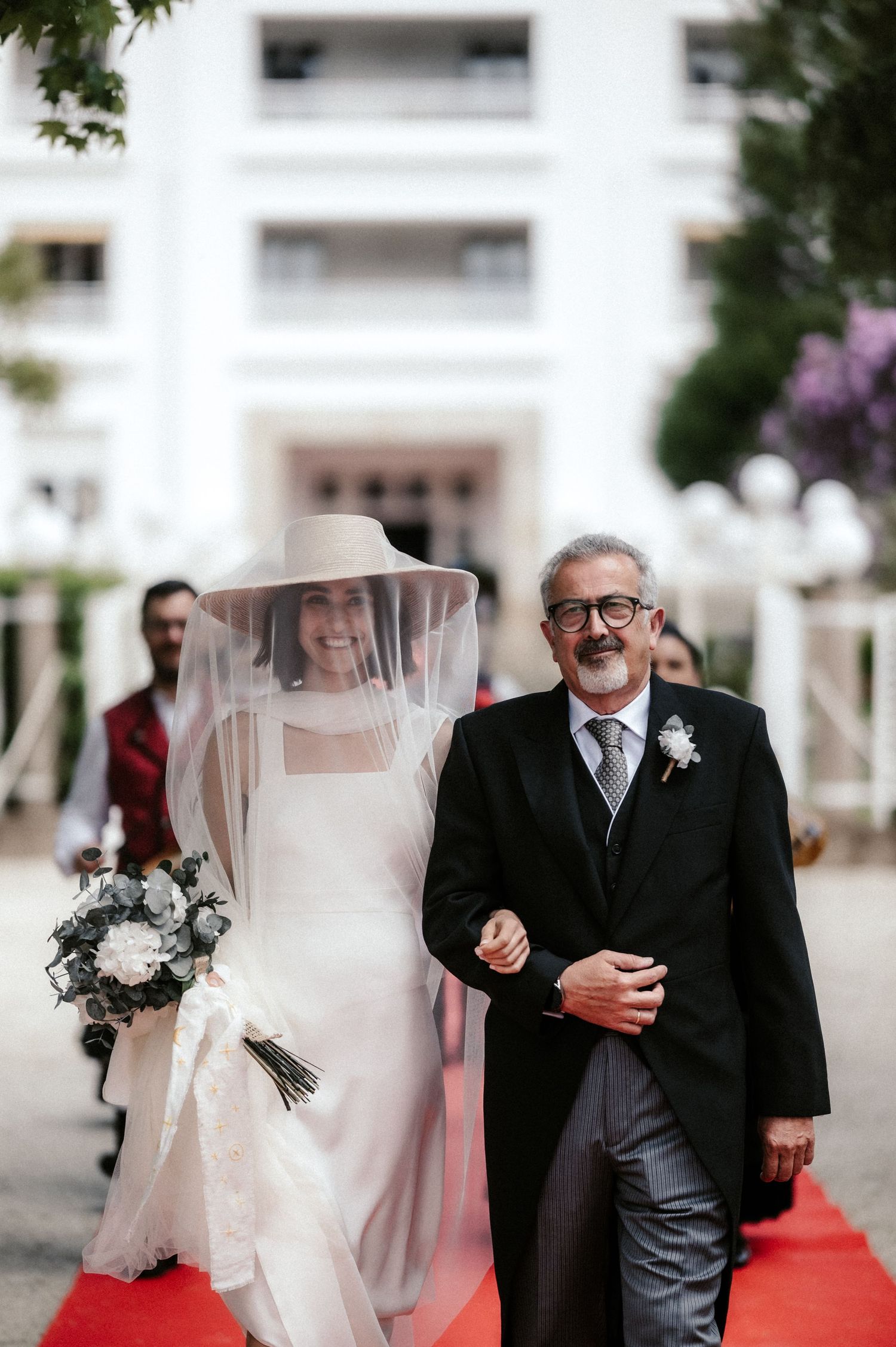 Elegant wedding ceremony on a red carpet with the couple walking together under a white veil.
