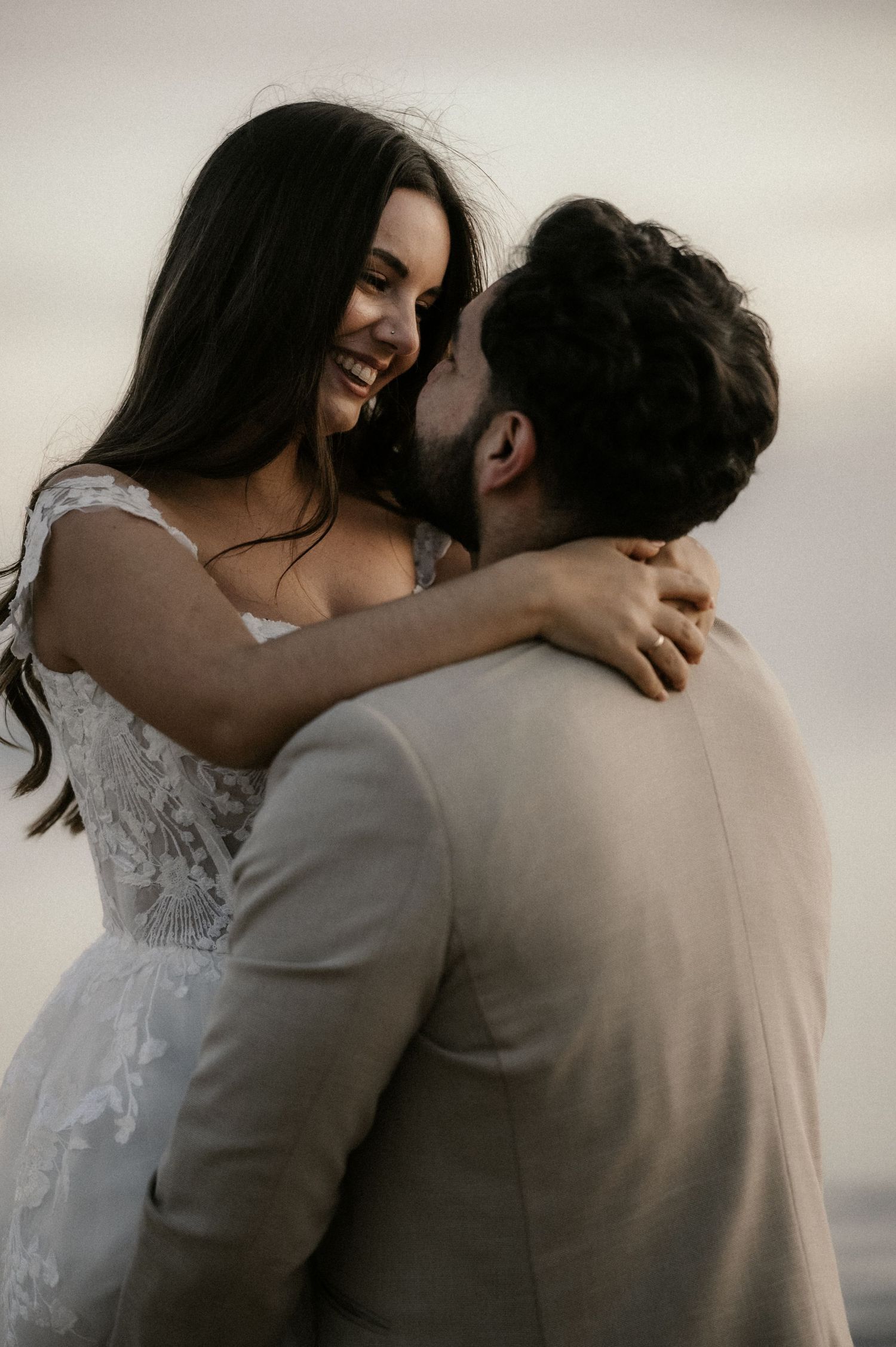 A couple in wedding attire shares an intimate embrace against a soft, muted background.