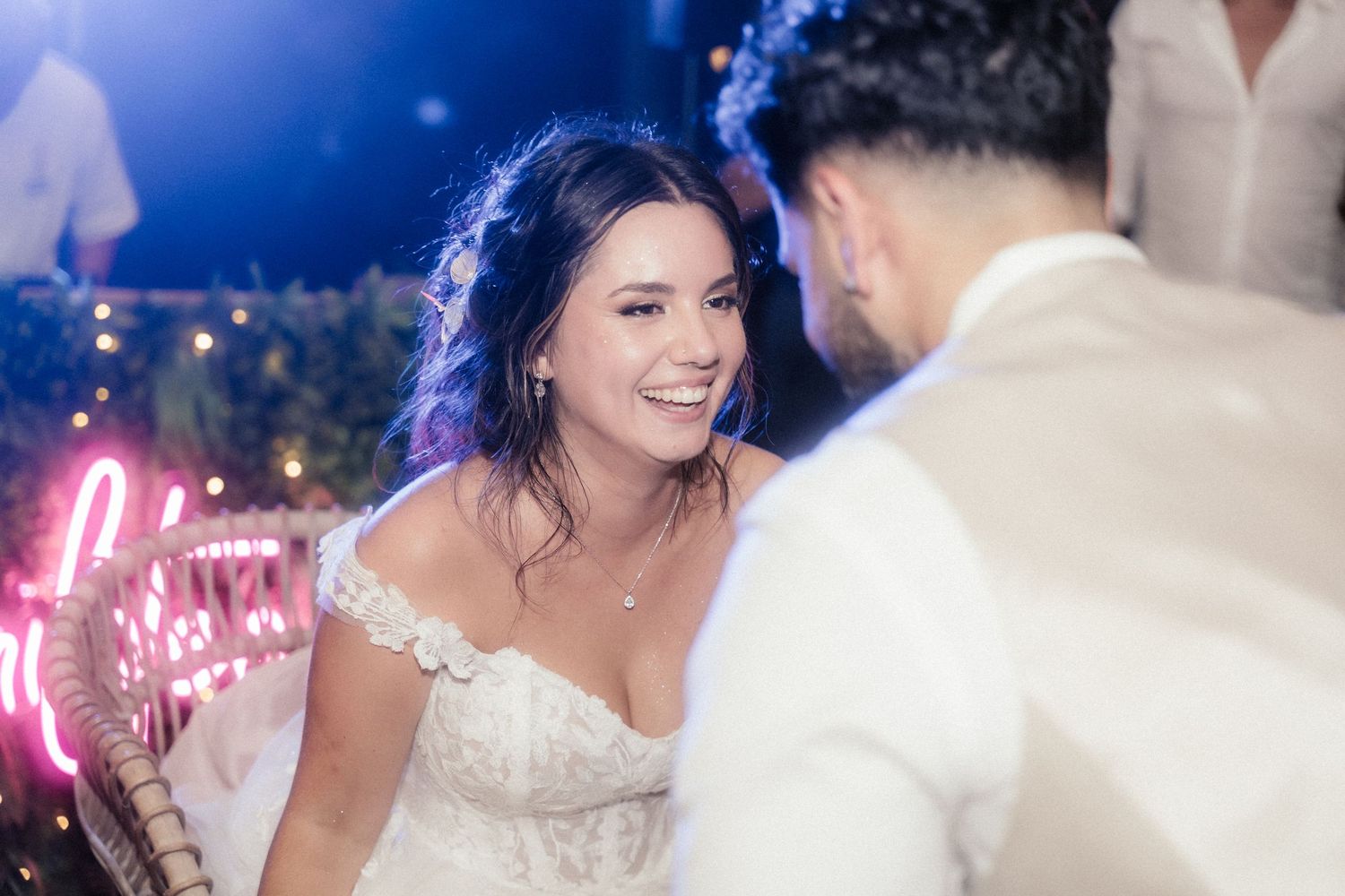 A couple shares a joyful moment on the dance floor with blue lighting and neon signs in the background.