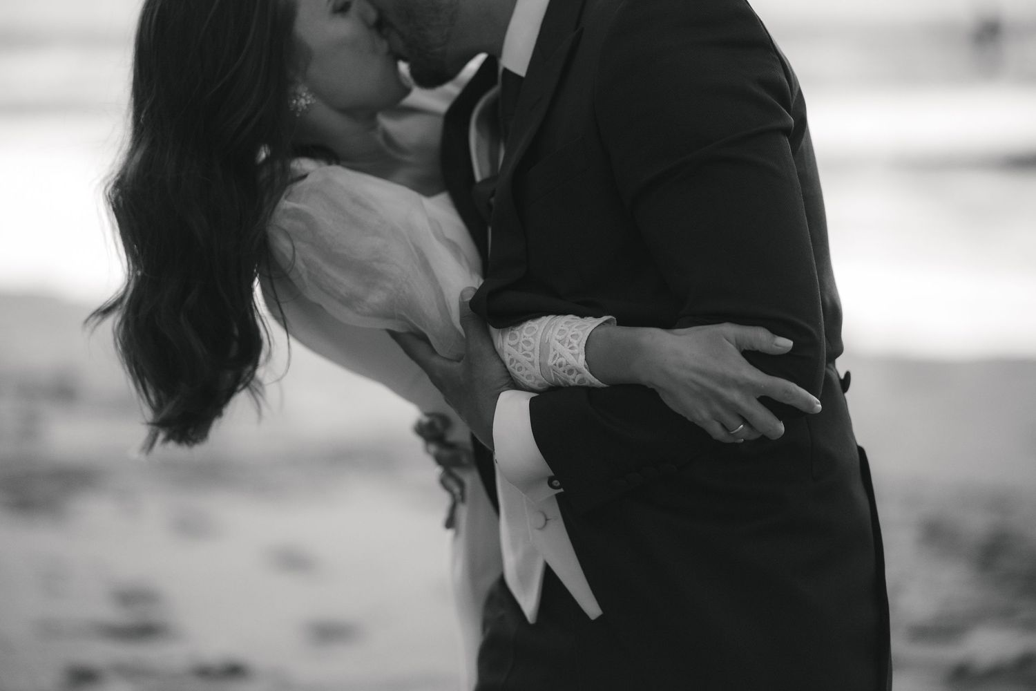 A romantic black and white photo shows a couple embracing and kissing on a beach.