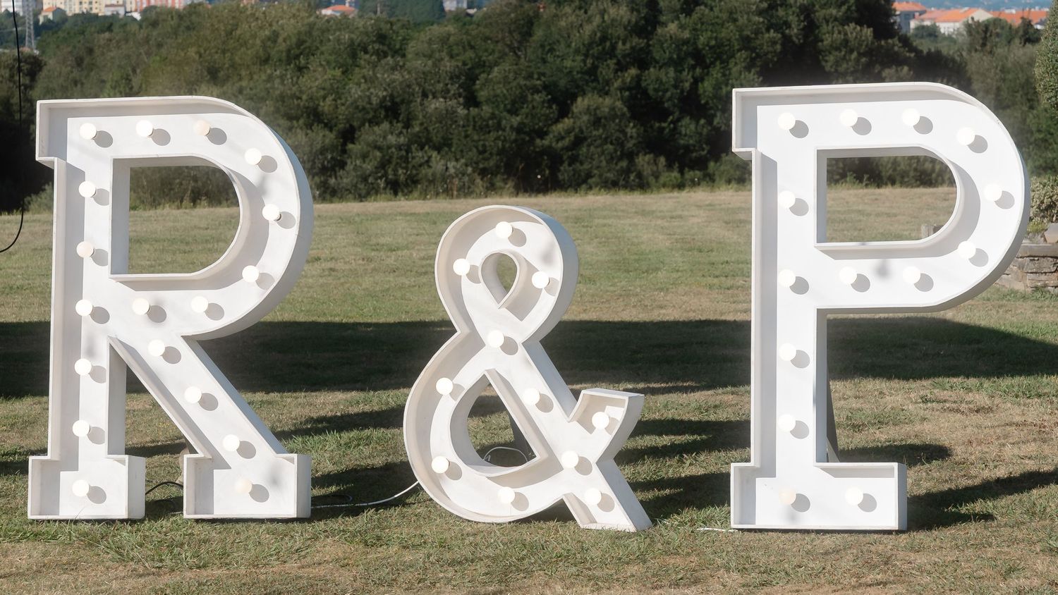 Large illuminated marquee letters spelling P&R sit on grassy terrain against a backdrop of trees and sky.