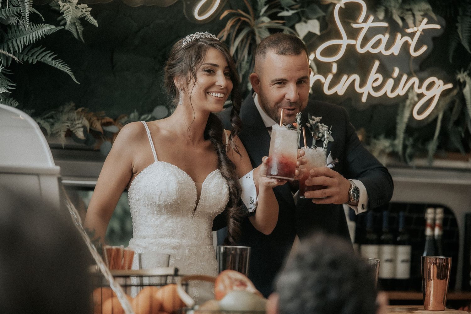 Wedding guests mingle and celebrate under glowing neon signage at a twilight reception.