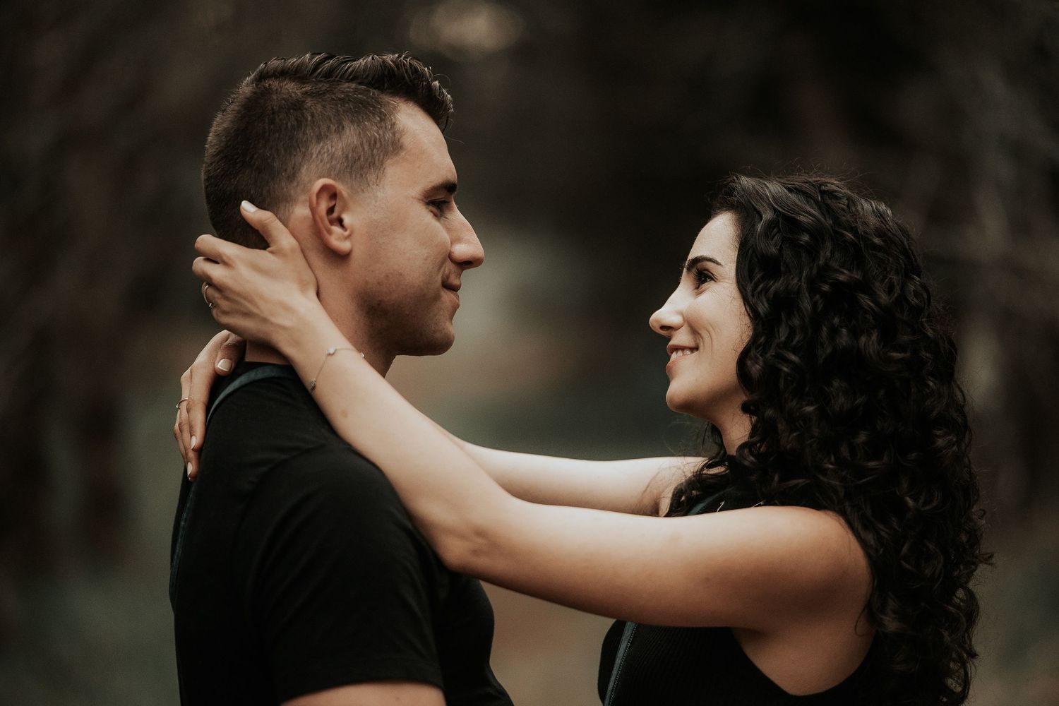 Romantic couple sharing an intimate moment while dancing together in a dimly lit forest setting.