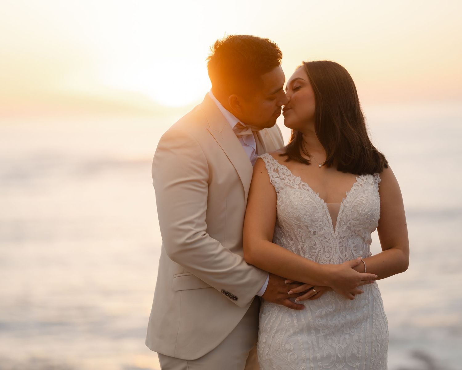 A romantic sunset beach portrait of a couple in elegant wedding attire.