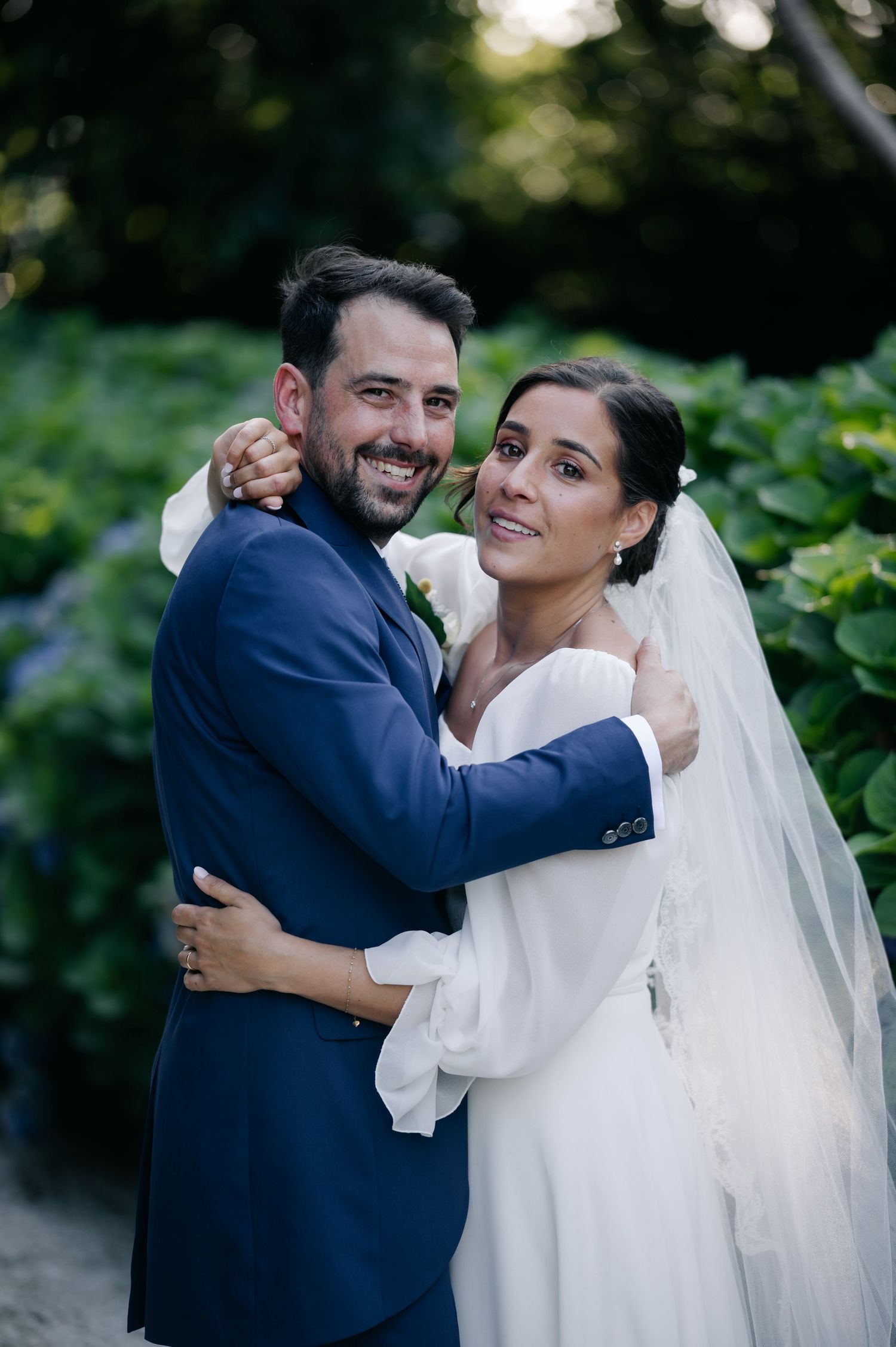 A joyful couple embraces outdoors during their wedding photoshoot with natural greenery in the background.