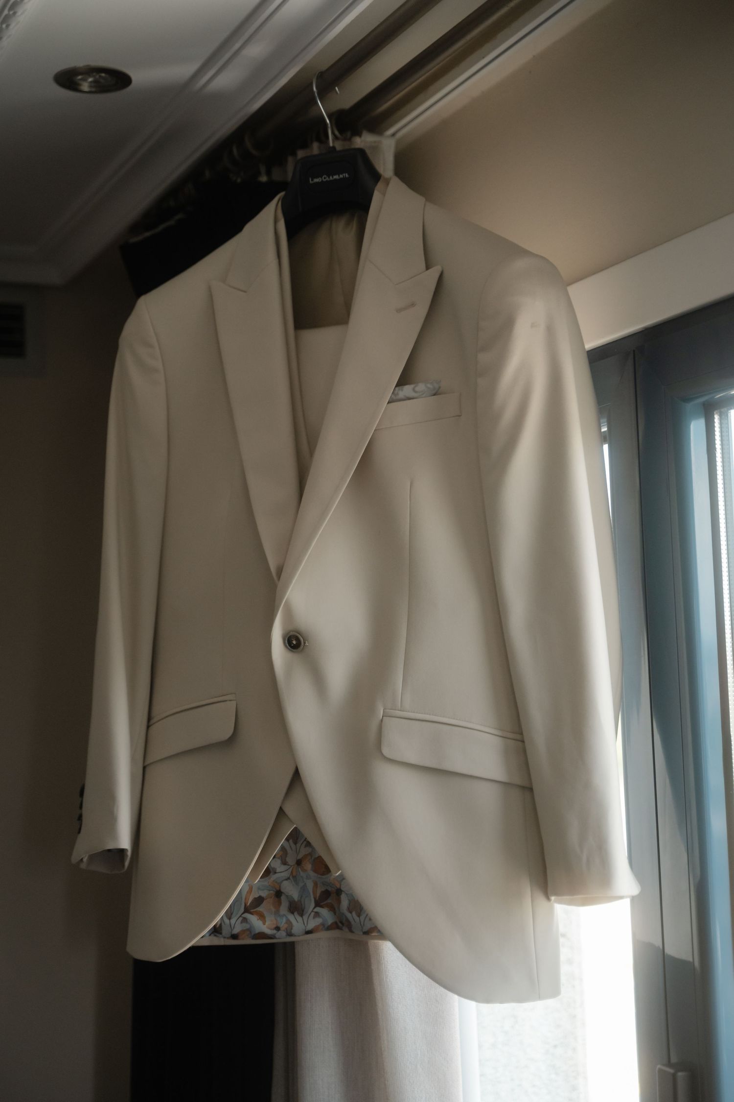 White formal blazer jacket hanging on display against a light colored wall with natural lighting.