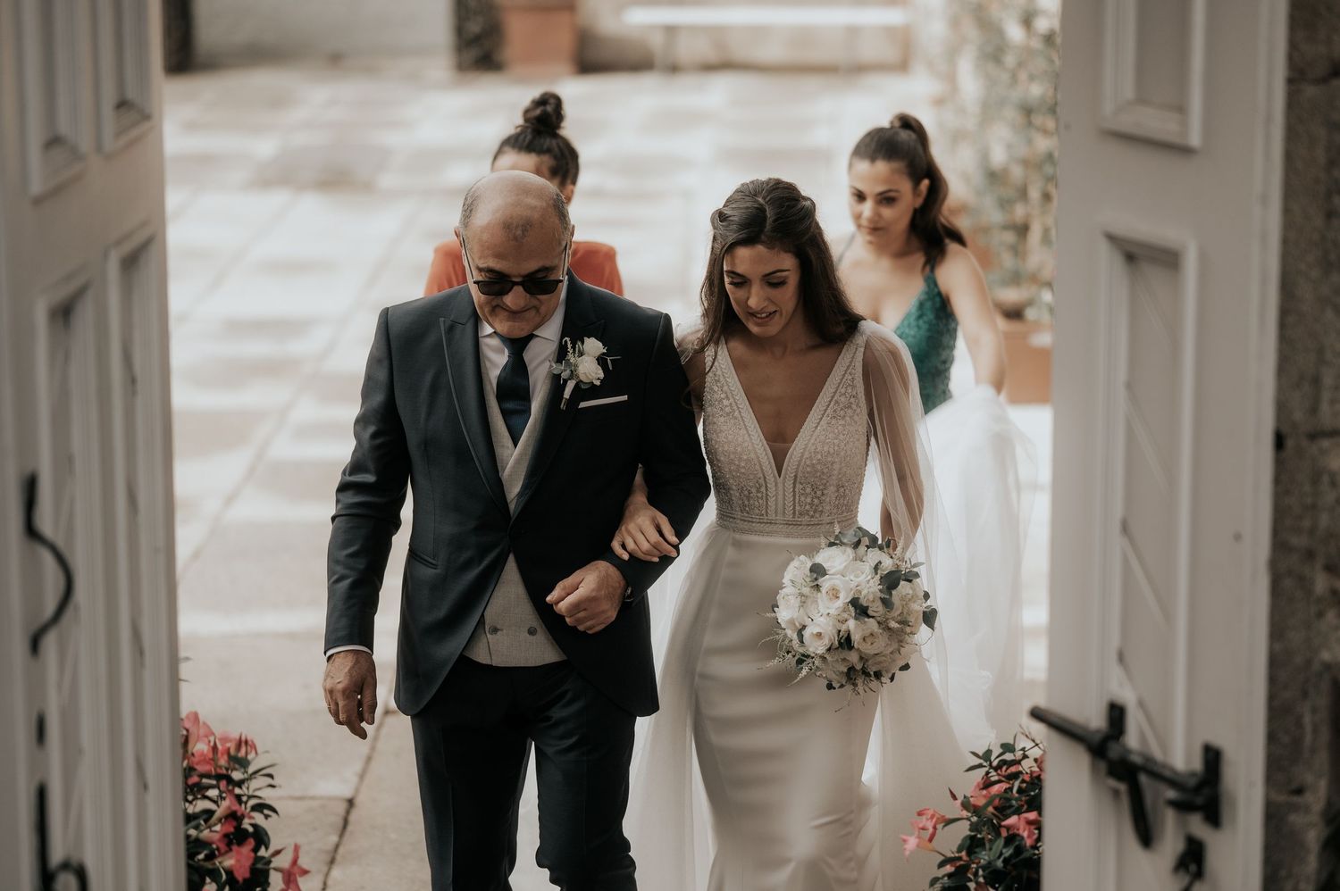 Wedding party walks down an elegant white hallway adorned with floral arrangements.