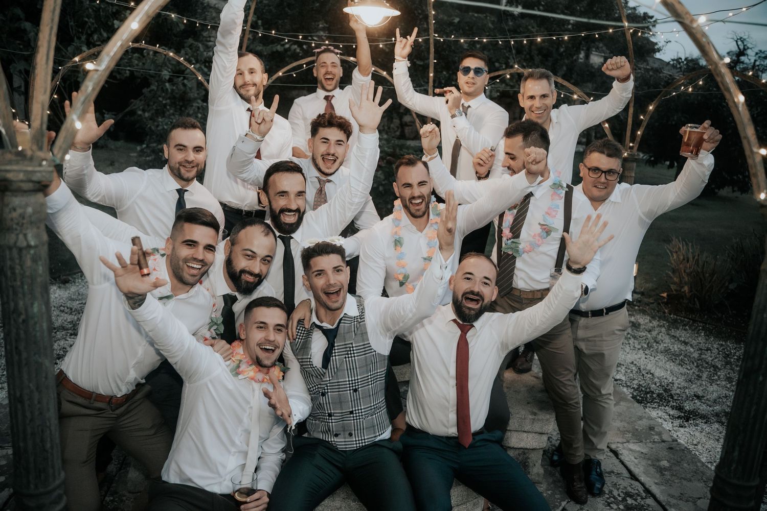 Wedding party members in white shirts and ties celebrating with raised arms outdoors.