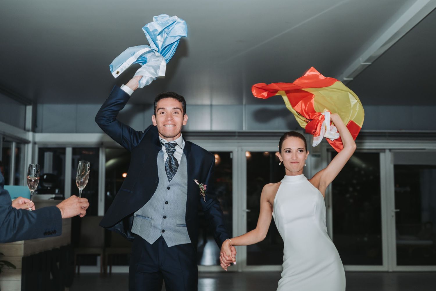 Wedding couple waves colorful handkerchiefs during a celebratory dance at an indoor reception venue.