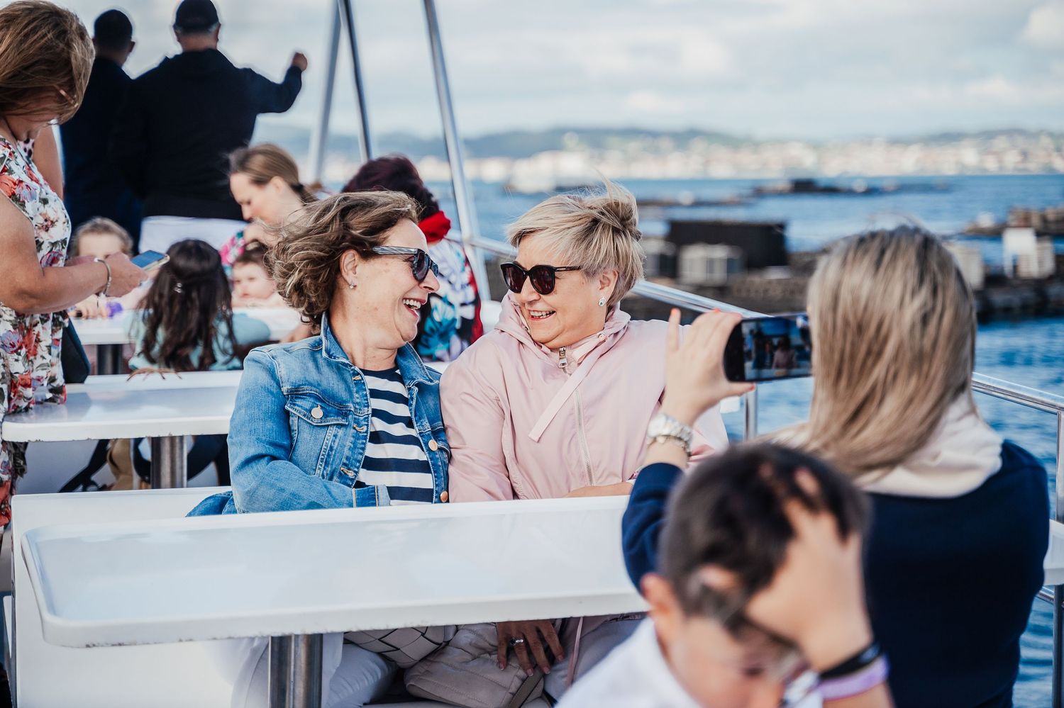 Friends enjoying drinks and conversation on a boat deck with ocean views in the background.