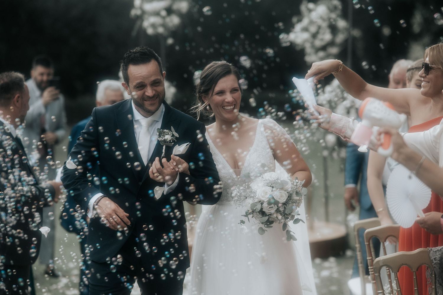 Newlyweds celebrate with guests as bubbles float through the air during outdoor wedding festivities.