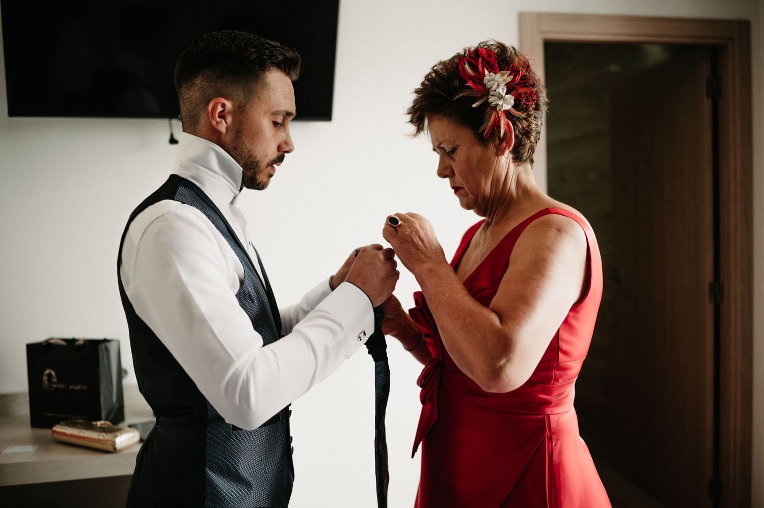 A couple shares an intimate dance moment in formal red dress and white shirt with suspenders at an indoor venue.