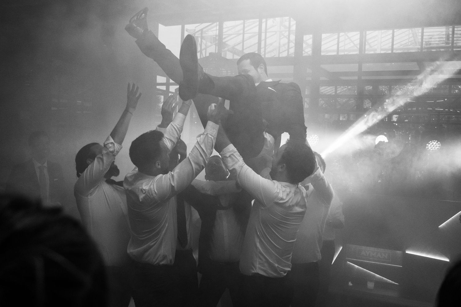 Silhouettes of wedding guests dancing with dramatic lighting and fog effects in a dark reception venue.