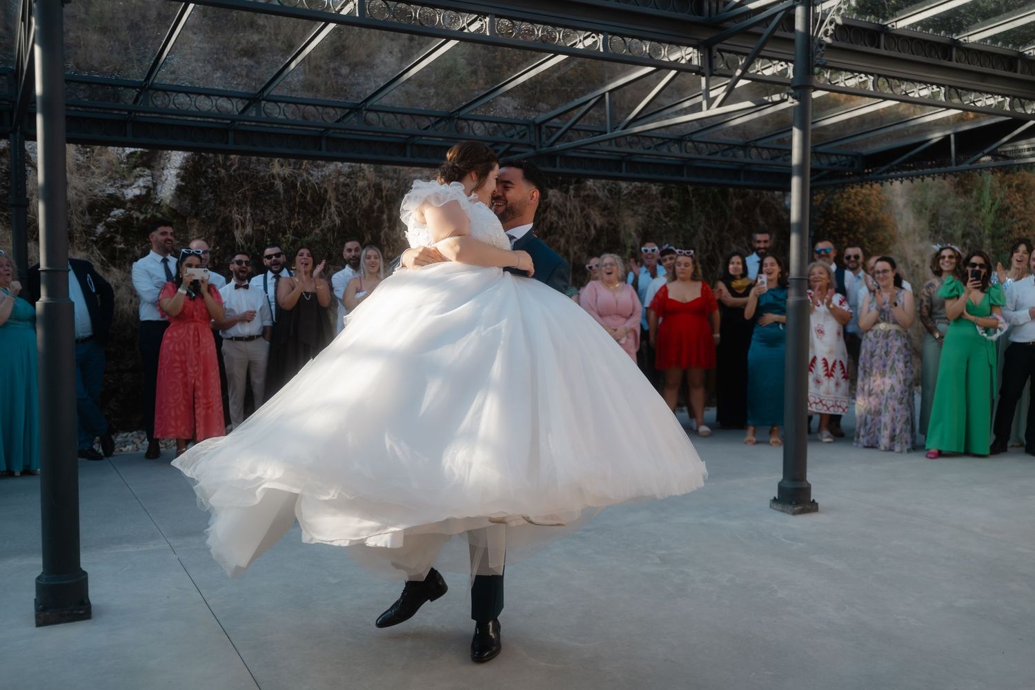 A bride in a flowing white dress spins gracefully on an outdoor dance floor surrounded by guests.