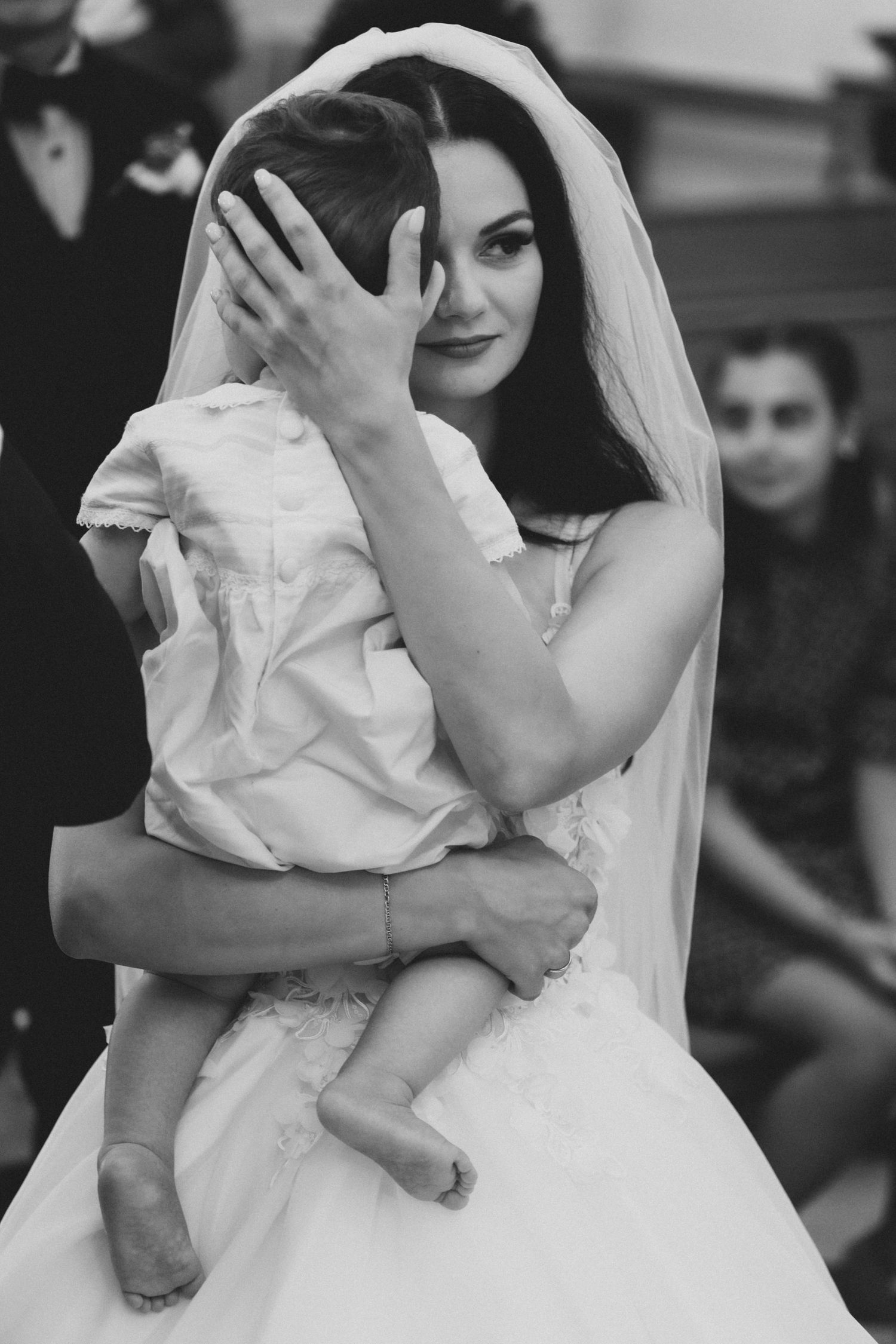 Black and white photo series showing a bride in a wedding dress holding a small child in four candid moments.