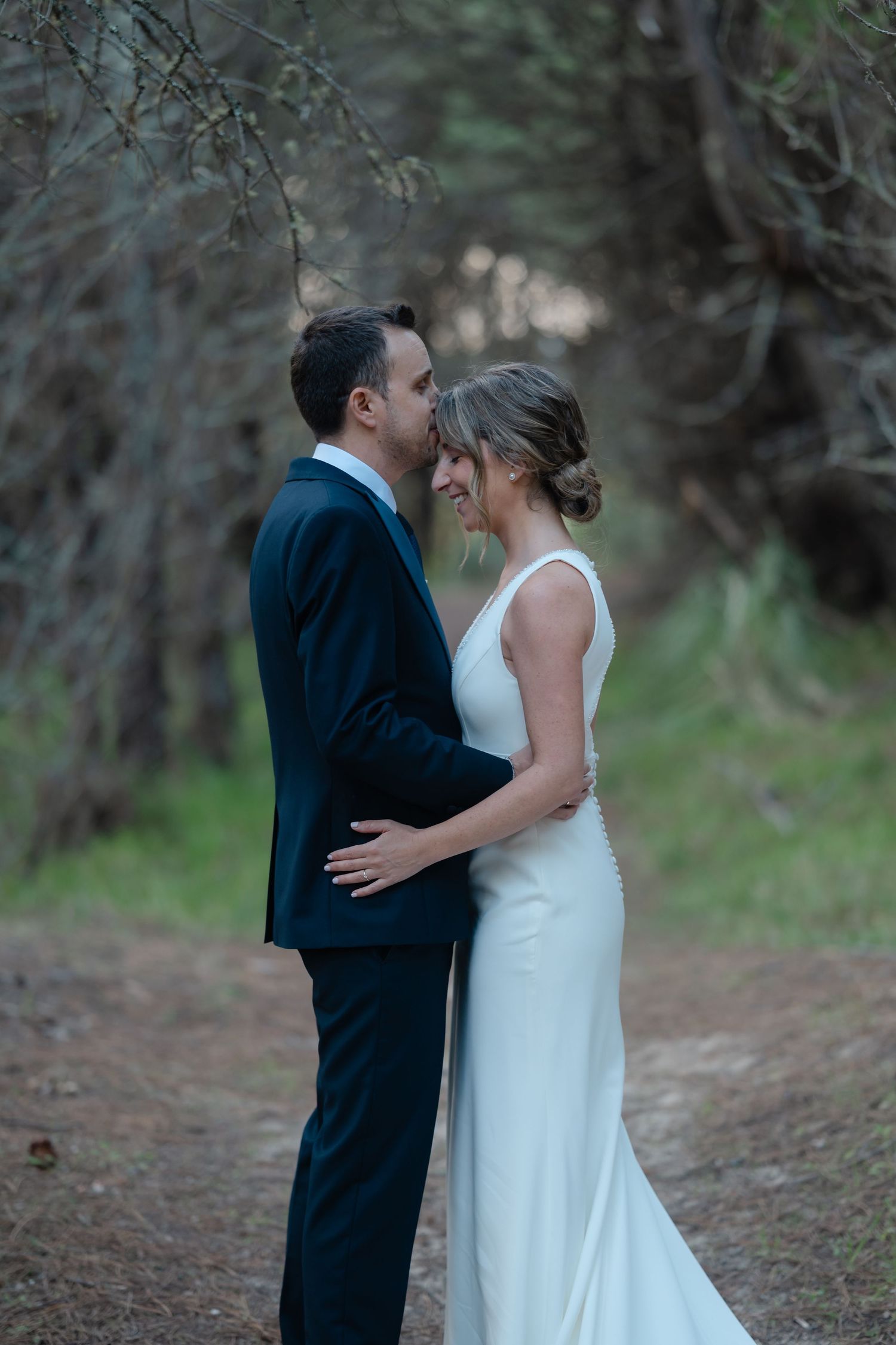 A romantic wedding couple embraces on a wooded forest path during their outdoor photo session.