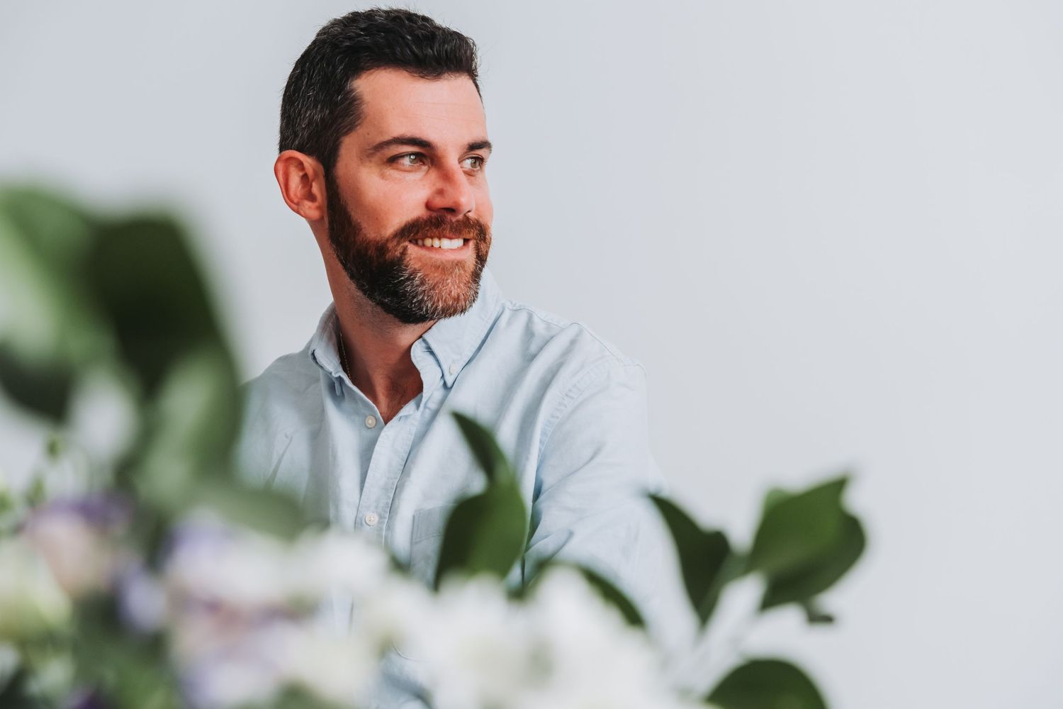 Professional wearing a light colored shirt smiles warmly in a bright office setting with green plants in background.