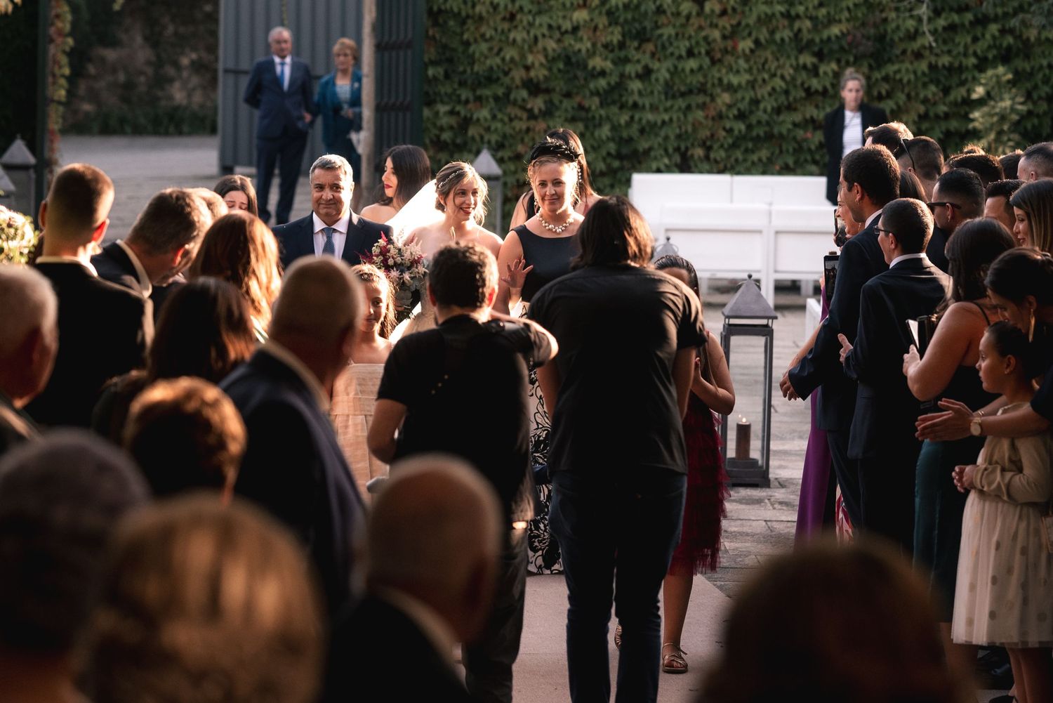 Wedding guests gather outdoors at dusk with string lights creating a warm ambiance for the celebration.