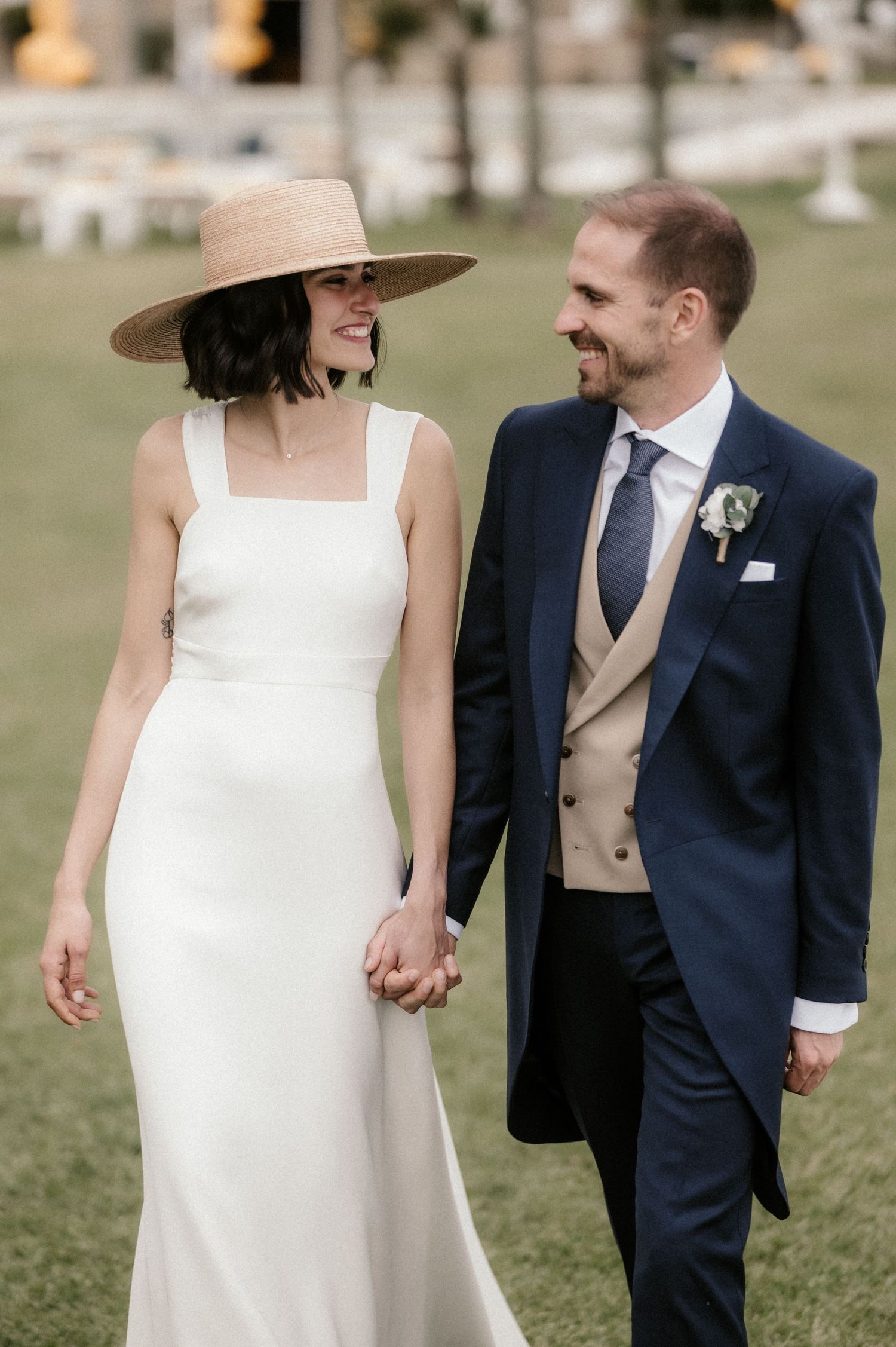Newlywed couple shares a joyful moment outdoors, bride wearing elegant white dress and wide brim hat.