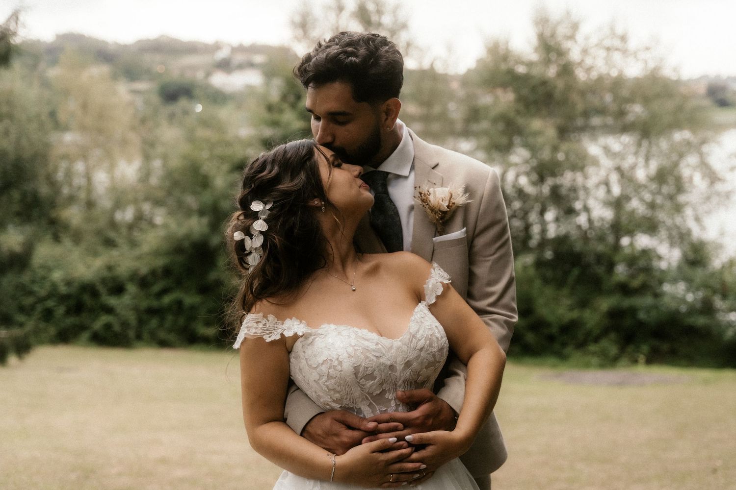 A romantic outdoor wedding scene with a couple embracing in a natural setting during golden hour lighting.